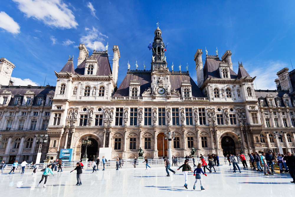 People ice skating in front of Hôtel de Ville on a sunny day in Paris in winter.