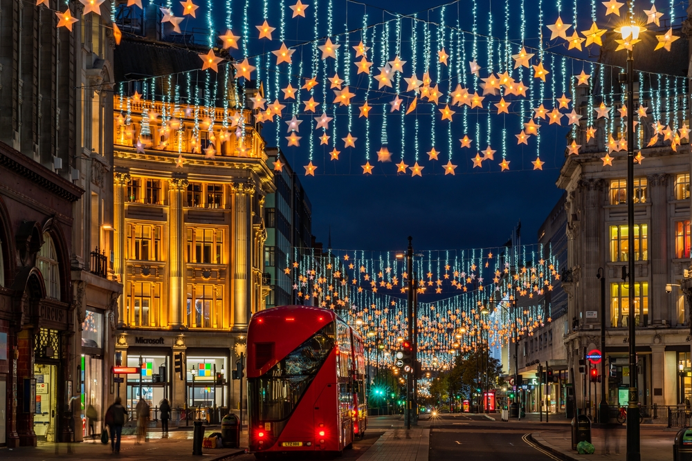 Night on Oxford Street in London with dangling stars strung between the buildings and a red double-decker driving underneath.