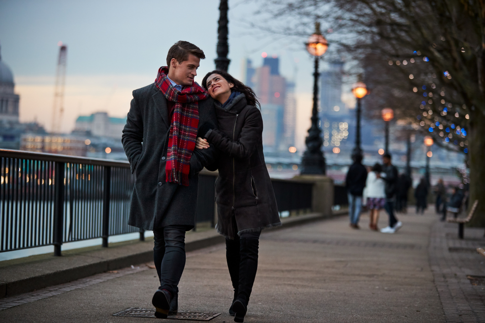 Couple dressed for winter walking along the river in London at dusk.