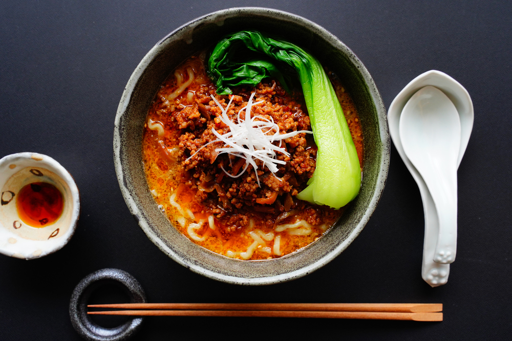 Looking down at a bowl of a classic Chinese soup with a white spoon, chopsticks, and a small bowl with a red sauce in it