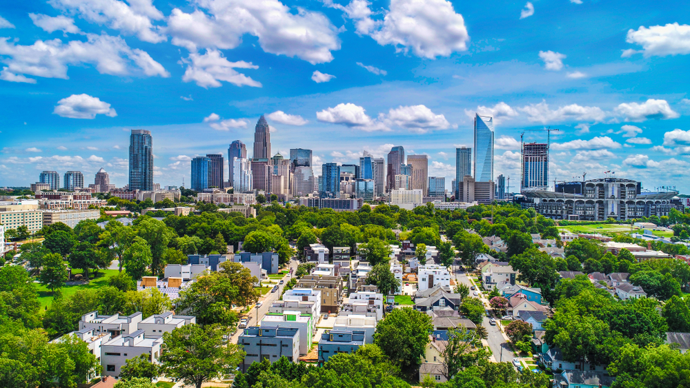 arial view of downtown Charlotte, during the day with partly cloud skies and green trees surrounding 