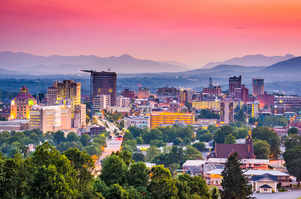 arial view of downtown Asheville at dusk with mountains in the background, surrounded by pink and purple skies 