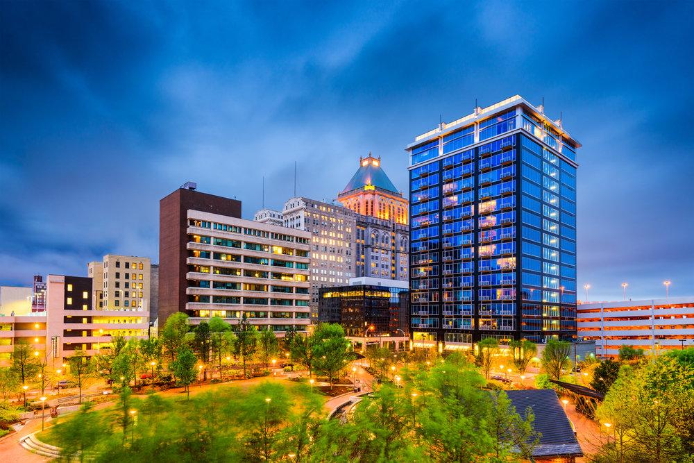 downtown Greensboro at night with the buildings glowing in the night sky and green trees at the bottom 