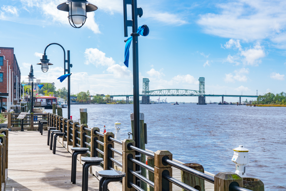 riverwalk pier located at cape fear river in Wilmington during the day with light posts tied with blue ribbon and seating places near the riverwalk barrier 