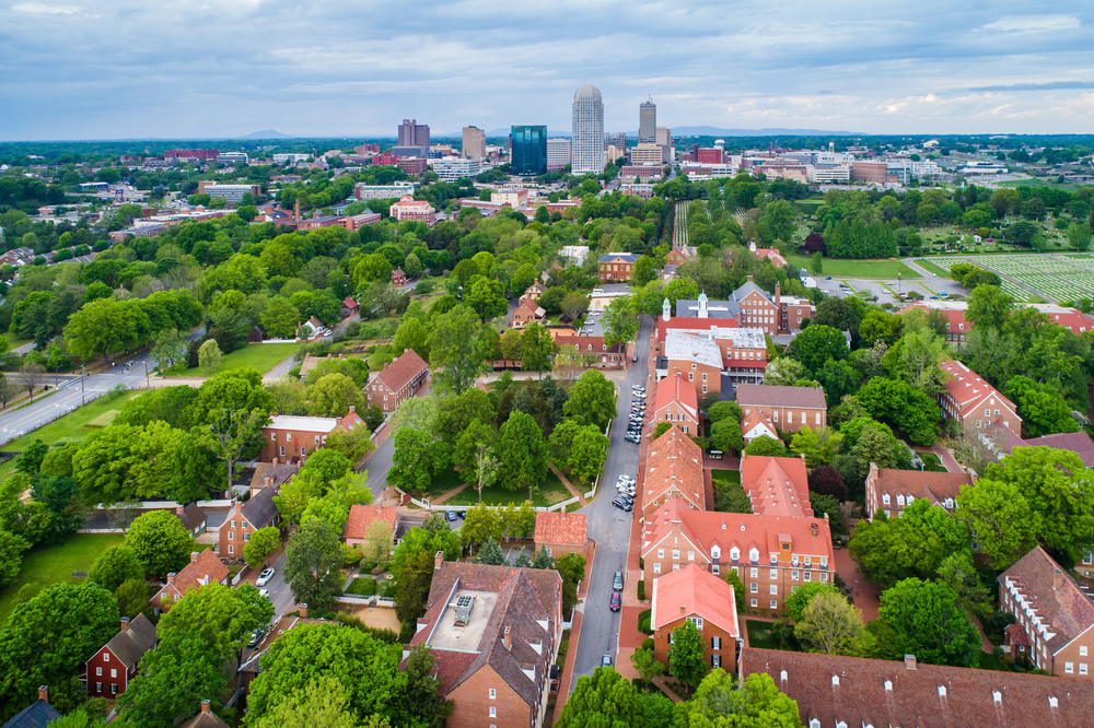arial view of historic downtown Winston-Salem with old brick buildings with bright red and brown roofs, surrounding green trees all over the town 
