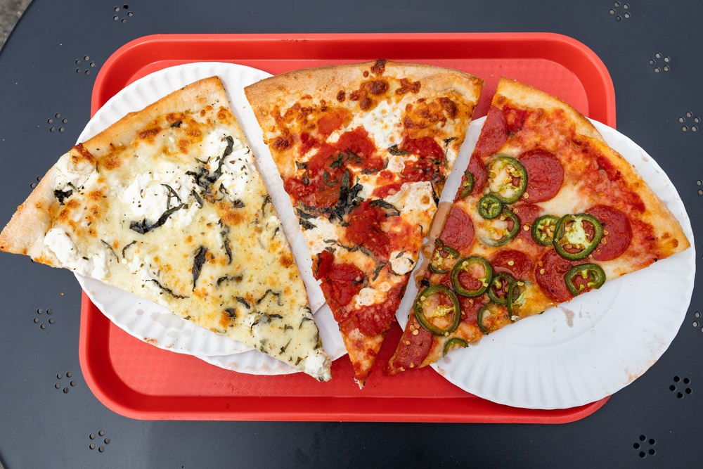 A red cafeteria tray with three different slices of New York style pizza