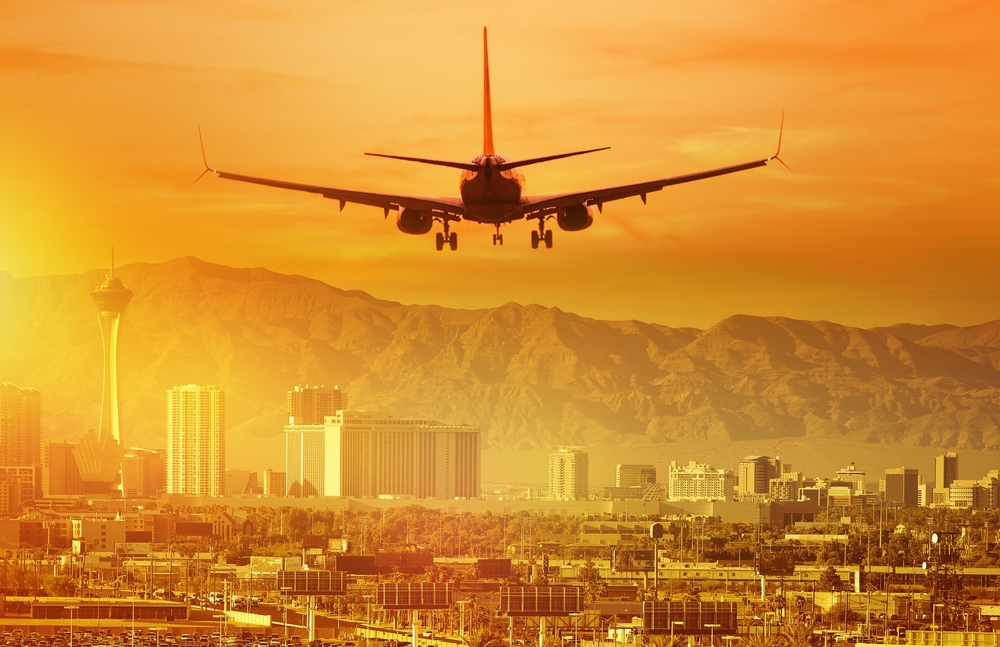 An airplane landing in Las Vegas with the city and mountains in the distance and the sky is orange from the sun setting