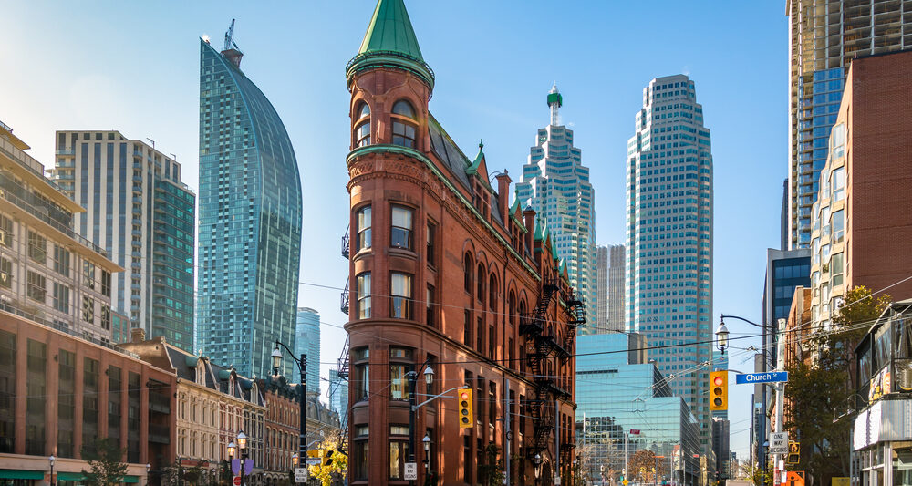 unique building that looks like a flat iron in downtwon Toronto with blue skies