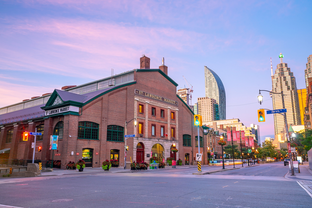 a dusky image of the older architechture of the St Lawrence market set in a street before massive, glossy and reflective skyscrapers. 