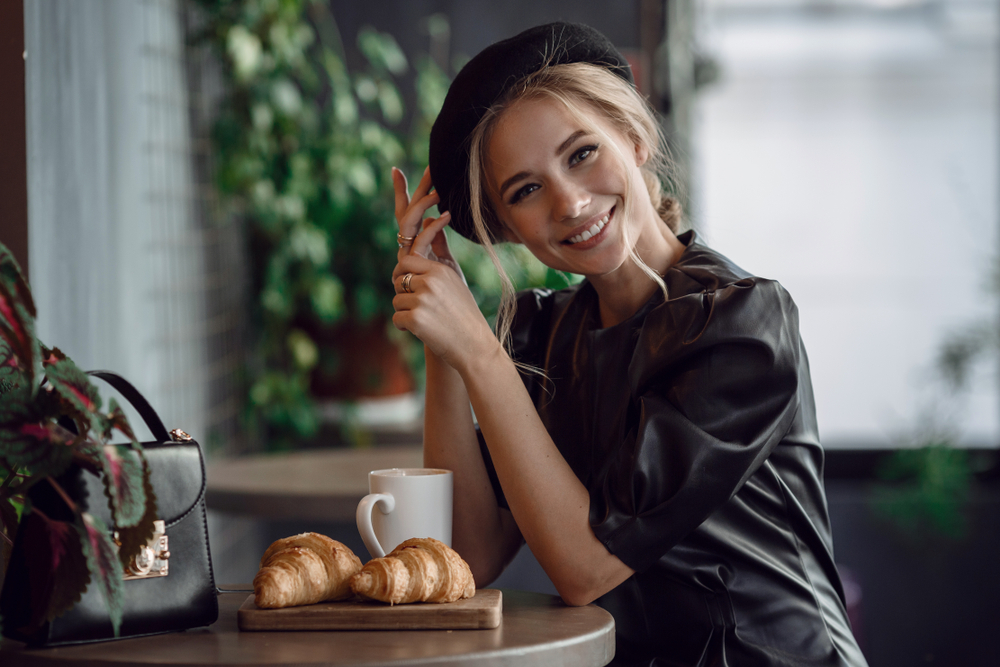 a girl in blacck is eating beakfast with croissants and coffee indoors