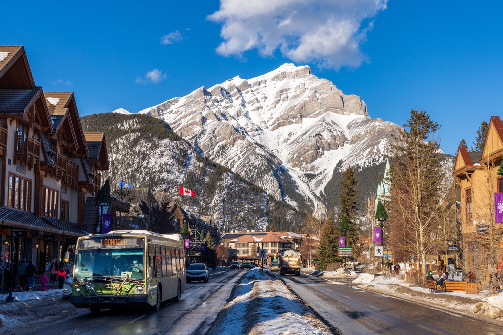 A bus driving through the Banff Center with a towering snow-capped mountain in the background.