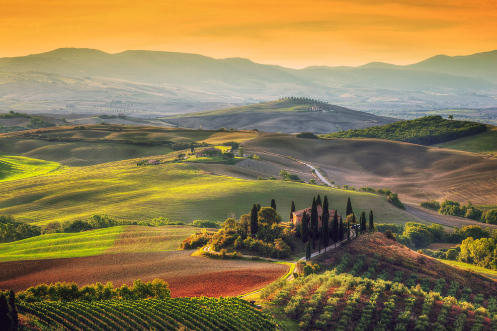 Aerial view of golden hour over the rolling green hills of Tuscany with a villa.