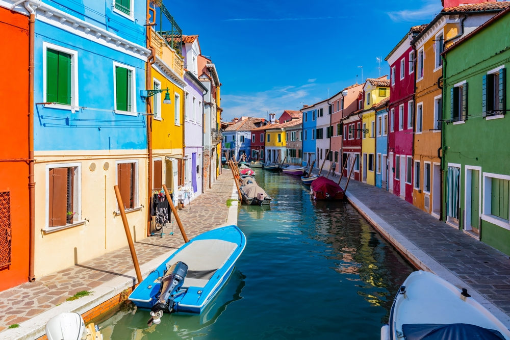 A canal with boats cutting through colorful buildings in Burano.