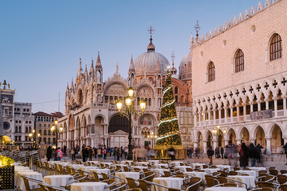 Dusk at St. Mark's Square with a tall Christmas tree next to the Doge's Palace and St. Mark's Basilica in the background.