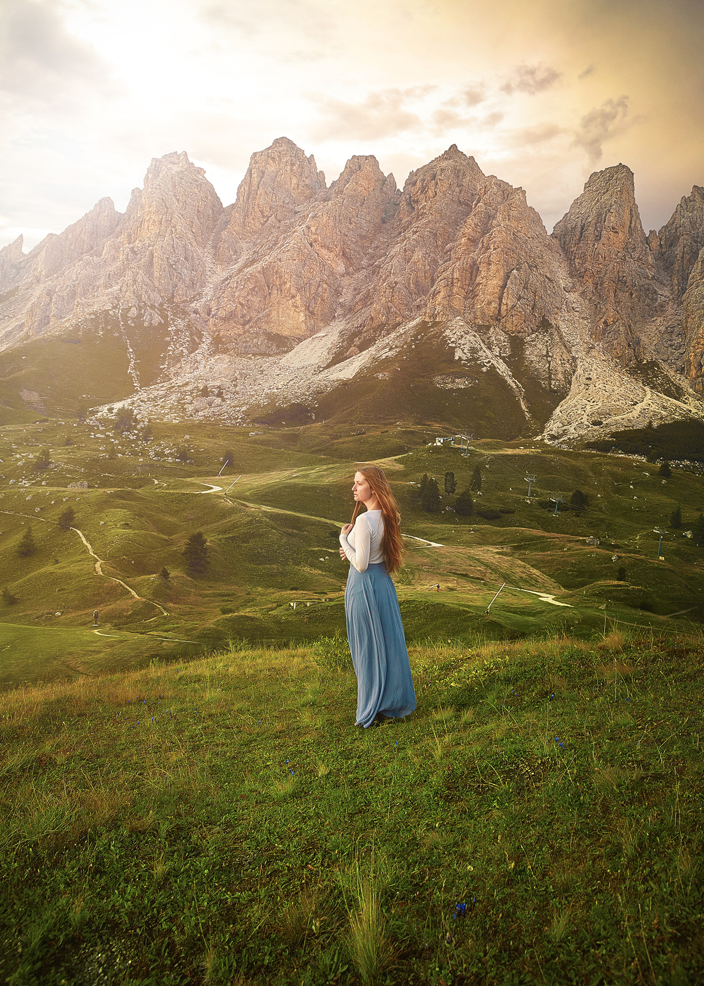 Woman in blue skirt standing in a field with the Dolomites in the background.