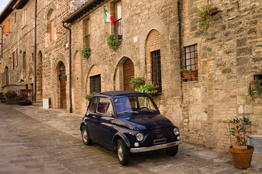 Small black car in a street with stone buildings in Italy.