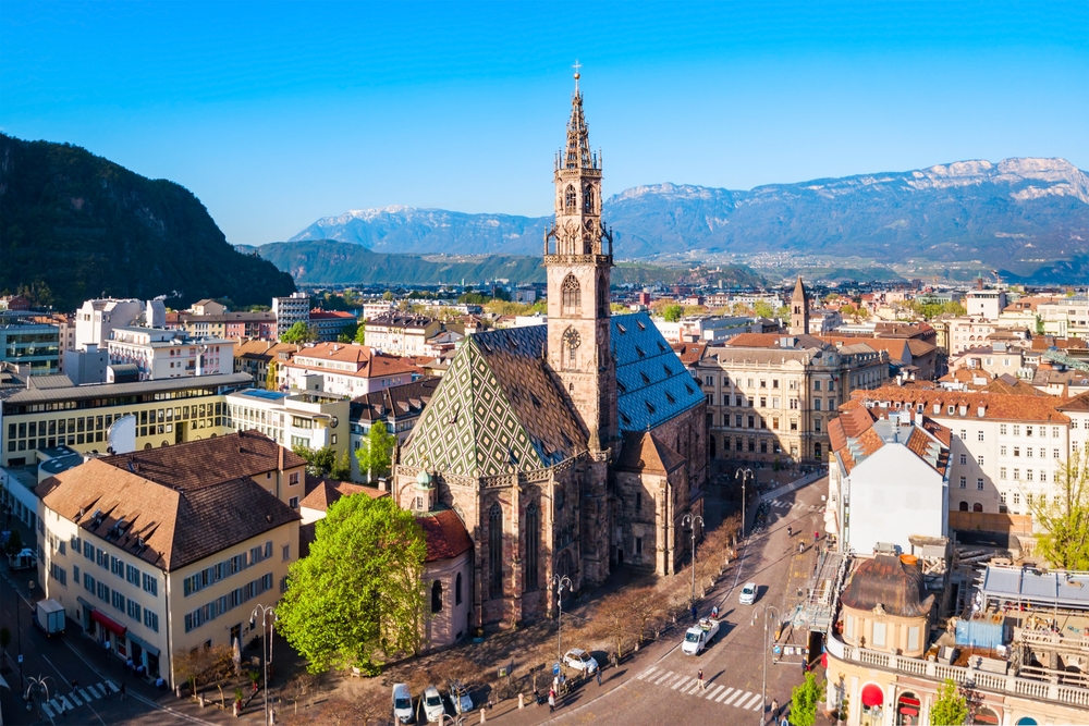 Aerial view of historic Duomo di Bolzano in a city with mountains in the distance.