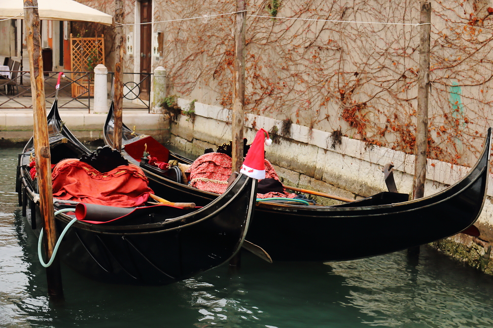 Two docked gondolas one with a Santa hat on the tip in Venice in winter.