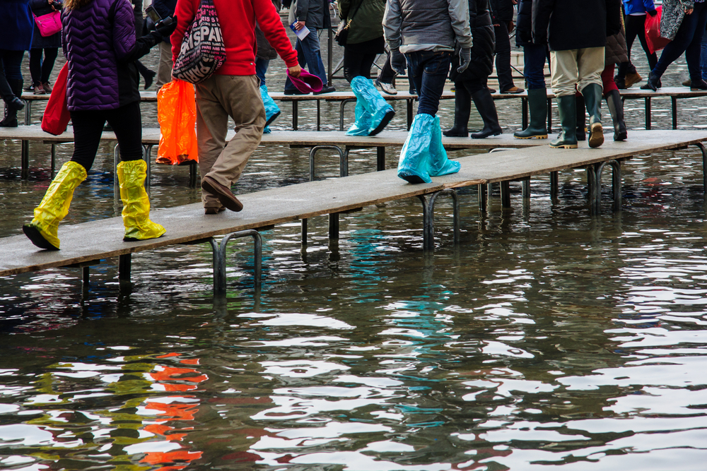 People in plastic booties and rain boots walking along a raised walkway in Venice in winter.