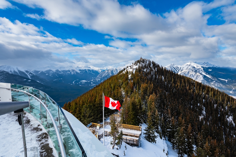 View from atop Sulphur Mountain with Canadian flag and snowy mountains.