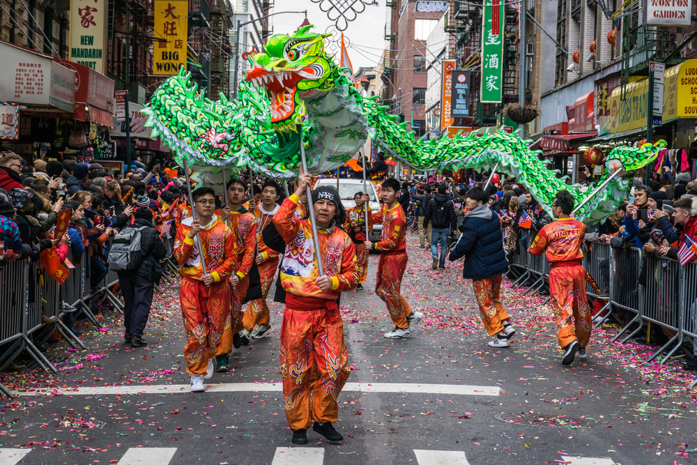 Men dressed in red holding a green dragon puppet in a parade in Chinatown.