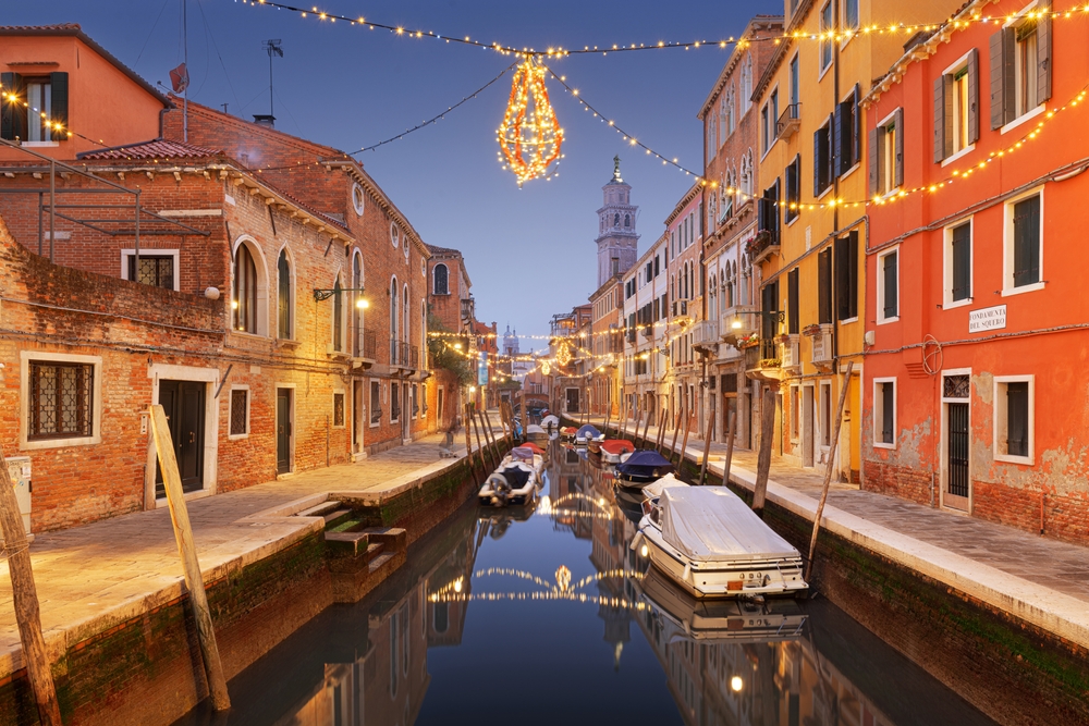 Christmas lights strung between buildings over a small canal in Venice in winter.