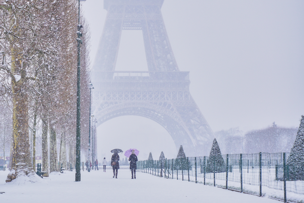 People walking with umbrellas under a snowfall with the Eiffel Tower in the background.