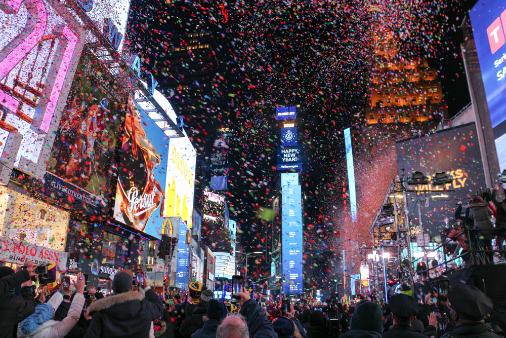 Confetti falling all around at night at Times Square with a giant crowd of people.