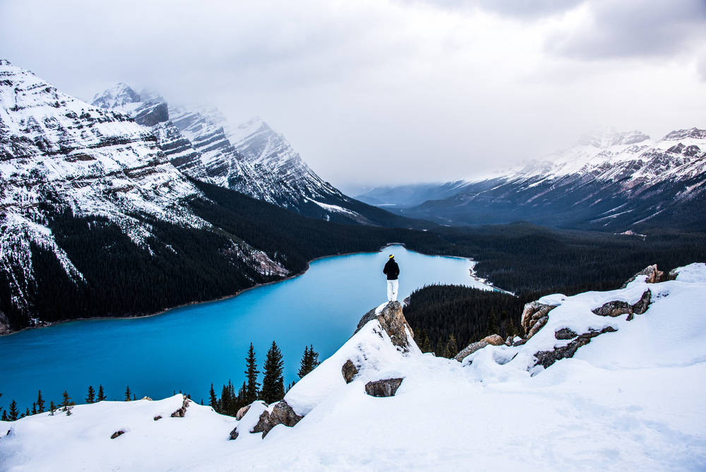 A figure on a rock overlooking Peyto Lake on a snowy day in Banff in winter.