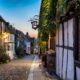 A charming cobblestone street in an old town of Rye England at dusk, flanked by traditional timber-framed buildings with warm glowing windows, inviting a sense of historical enchantment.