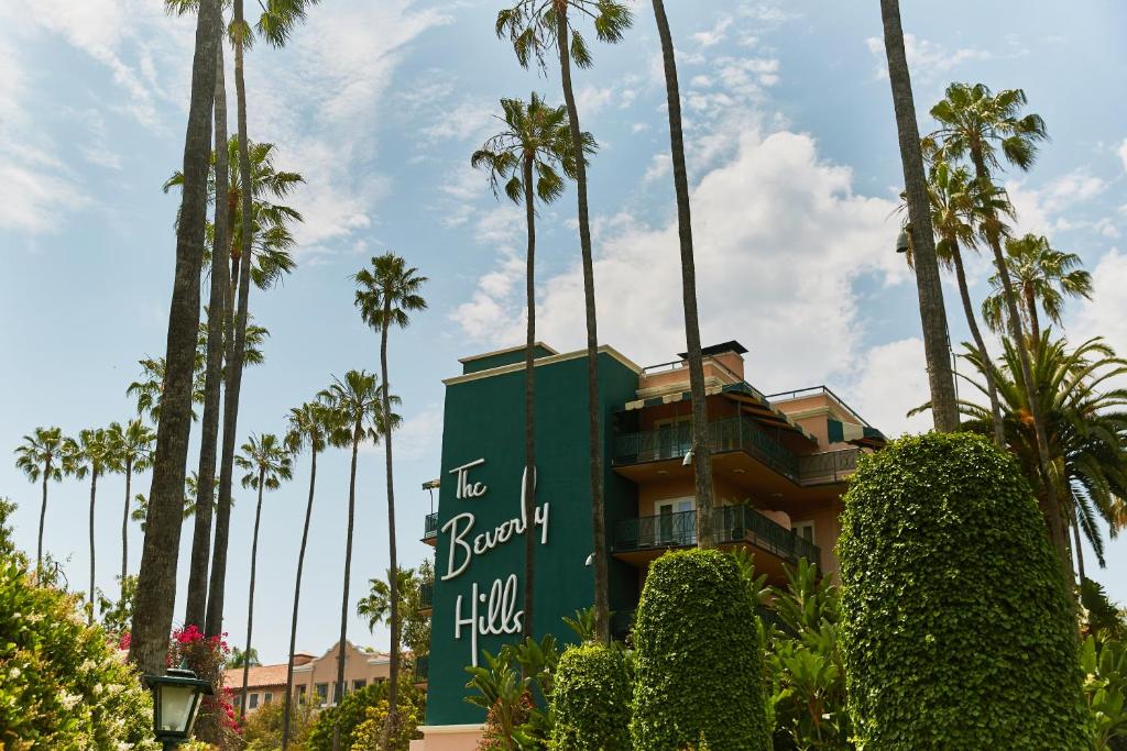 The Beverly Hills Hotel sign on the side of the hotel with palm trees in front of it. 