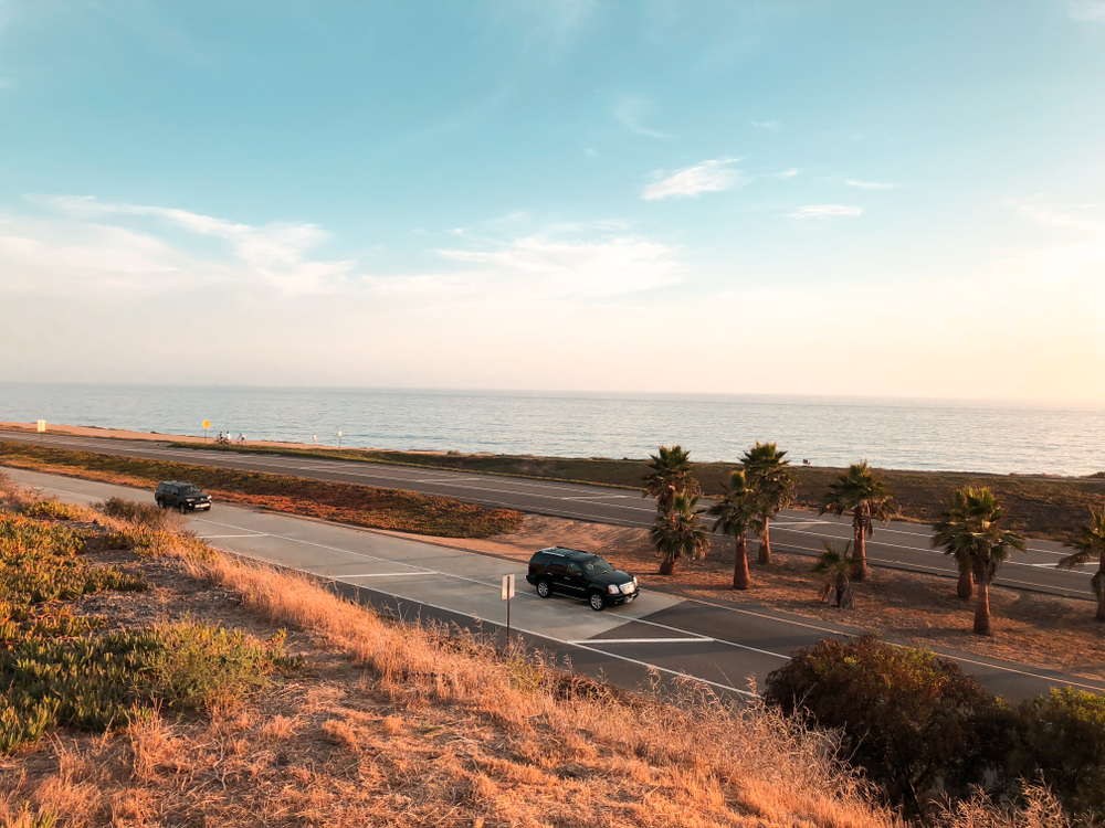 Cars driving down The Pacific Highway with palm trees and the sea to the side. 