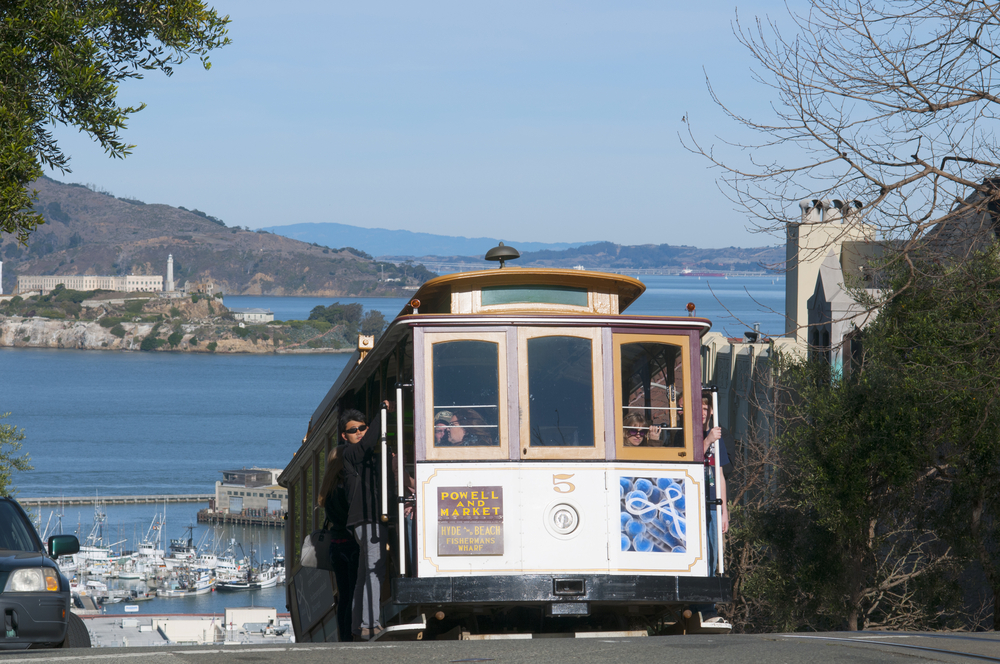 Powell street cable car going up the road with the harbour in the background.