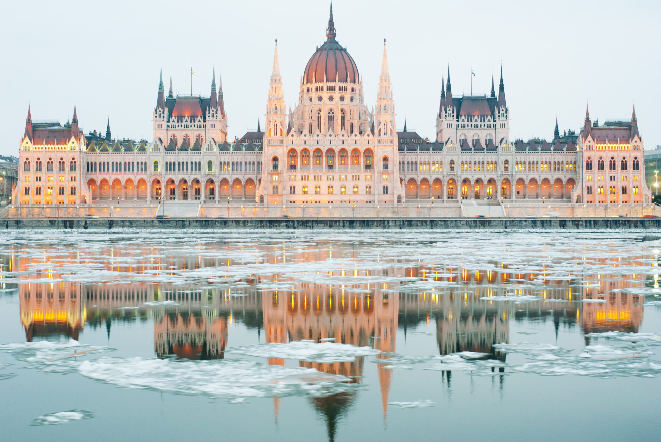 Budapest parliament lit of up at night with ice on the river below and grey sky