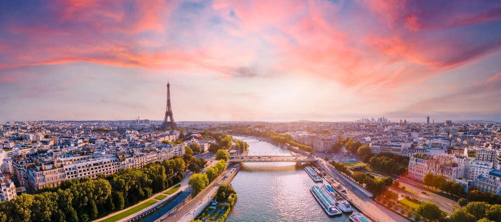 An Ariel view of Paris at sunrise with cotton candy colored clouds, Seine River, Eiffel Tower and Louvre can all be seen
