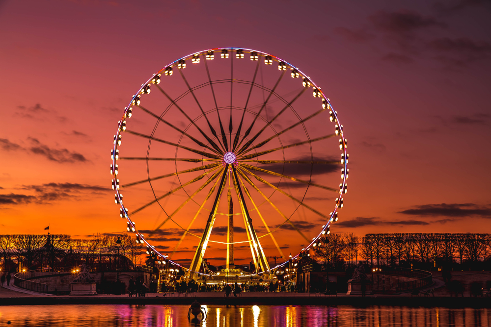 The iconic Paris Ferris wheel at sunset illuminated orange sky with lights