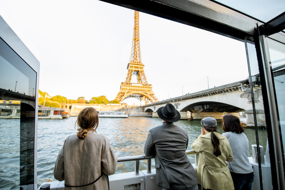 a group of people standing outside on a boat tour down the Seine River overlooking the Eiffel Tower