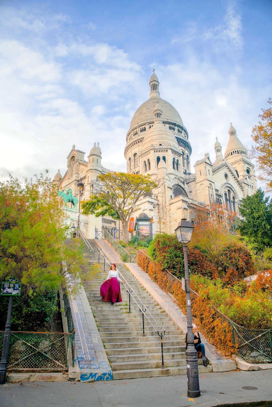 a girl in red skirt standing on the steps with Sacre Coeur in the background
