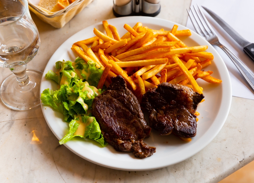 a typical French meal of steak, fries, salad with bread and wine