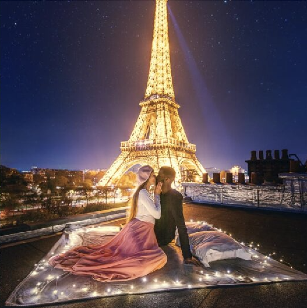 The sparkling Eiffel tower with a couple surrounded by lights on a rooftop in Paris