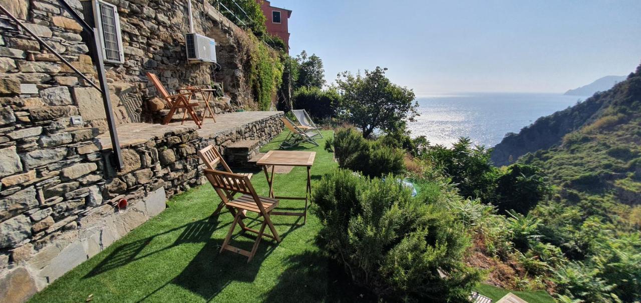 Wooden tables and chairs in a cliff-side garden area with the sea in the distance.