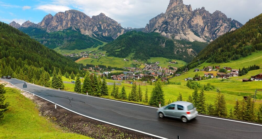 car driving along the dolomites in italy with green rolling hills and mountains