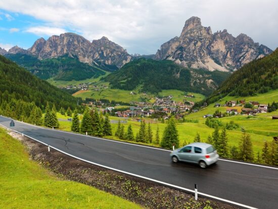 car driving along the dolomites in italy with green rolling hills and mountains