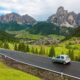 car driving along the dolomites in italy with green rolling hills and mountains