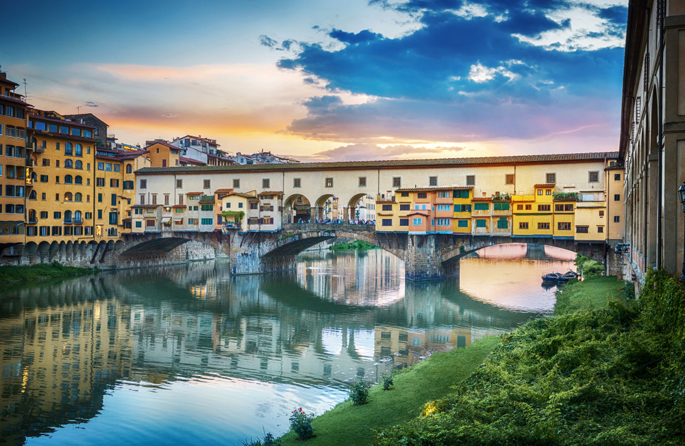 Sunset over the colorful Ponte Vecchio bridge reflecting over the water.