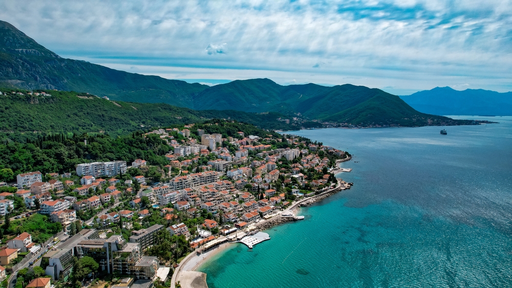 the seaside town of Herceg Nova in Montenegro. There are big mountains over looking the sea and plenty of greenery in the back. this is one of the best summer destinations in Europe! 