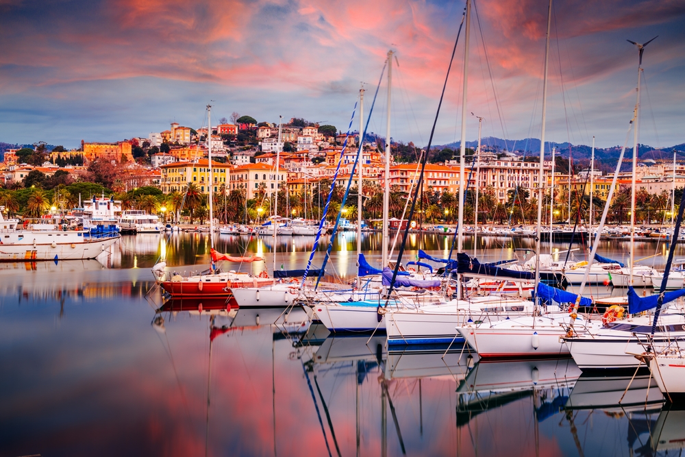Vivid sunset over the harbor with many sailboats with the city of La Spezia in the background.