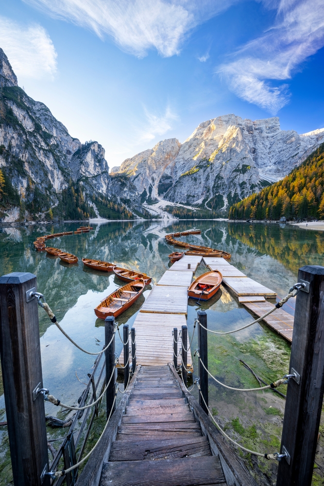 Lago di Braies lake with a line of wooden boats and docks at the base of rugged mountains on an Italy road trip.