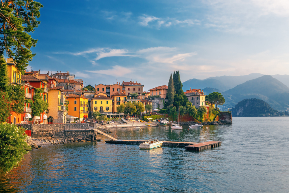 View of Lake Como next to colorful buildings and rolling hills in the background.