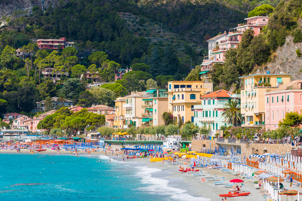 Beach covered in lounge chairs next to colorful buildings on a sunny day in Monterosso.